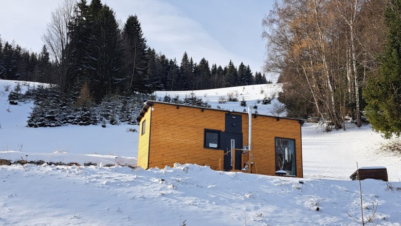 The "Villa to go" on the former lift slope, © Villa to go Small wooden house in the snow in front of a forest.