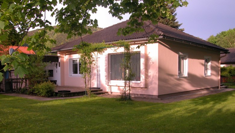 A pink-painted vacation home with a dark roof, surrounded by a green garden and trees.