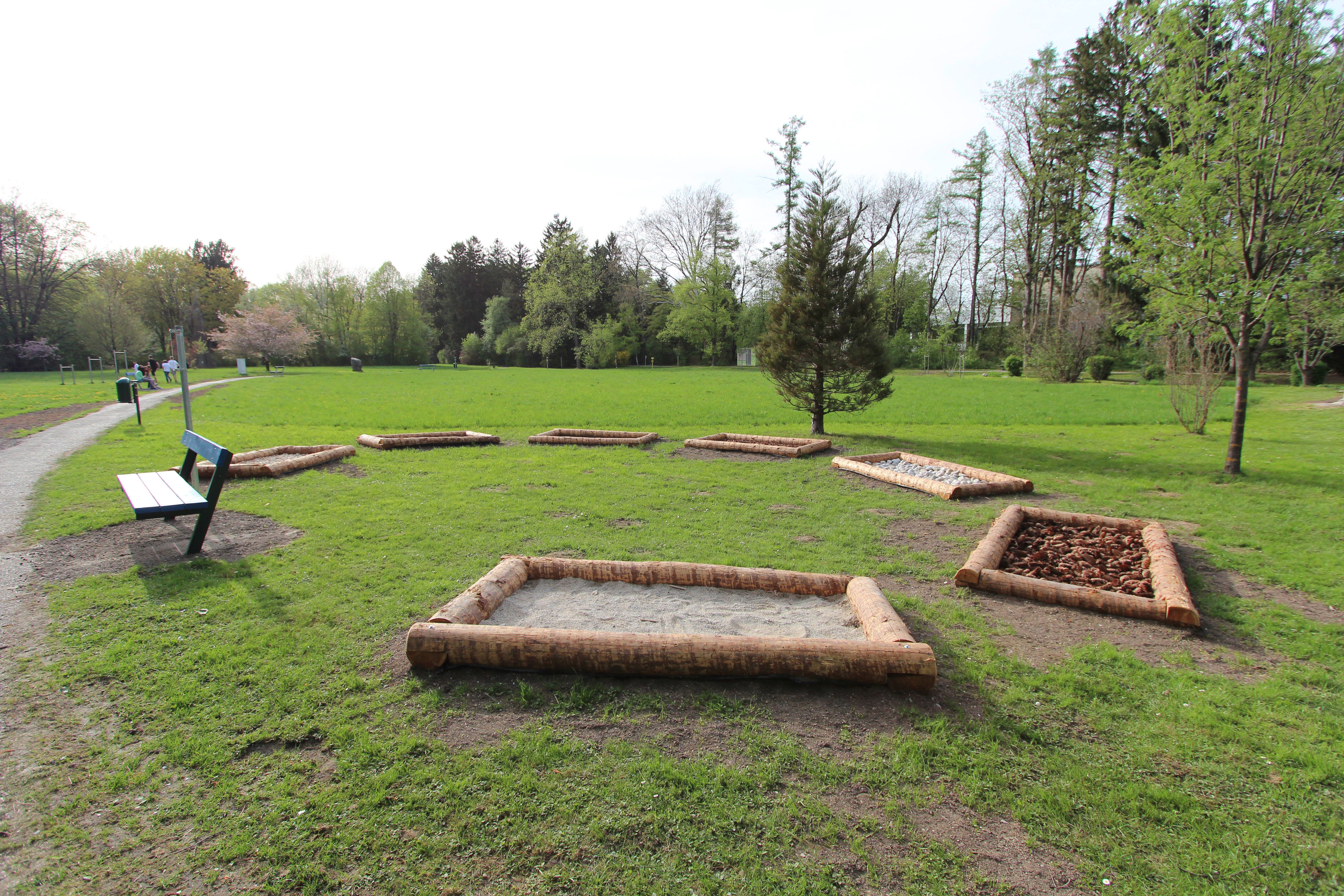 A city park with a barefoot path made of various materials and a park bench.