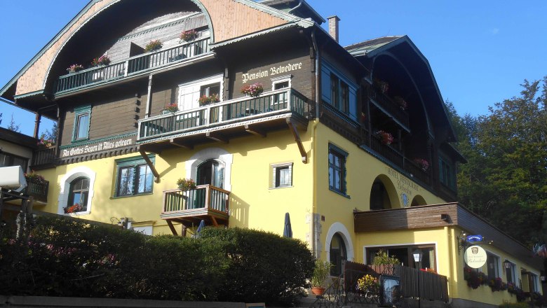 A traditional hotel with a yellow façade and wooden balconies, decorated with flowers.