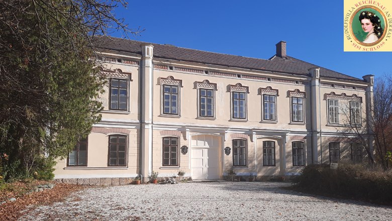 Sisi Palace Rudolfsvilla in Reichenau, two-storey building with light-colored paint and decorative windows.