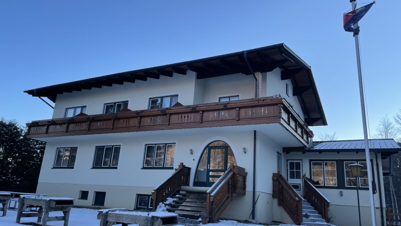 Bed and breakfast Mariahilfberg, © Weiner Alpen A two-story building with a wooden balcony and stairs, surrounded by snow, under a clear sky.