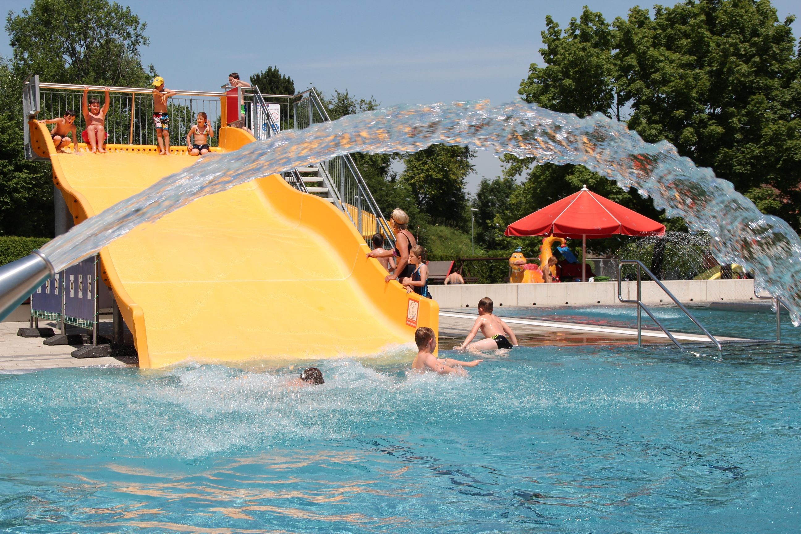 Children playing on a yellow water slide in an outdoor pool.