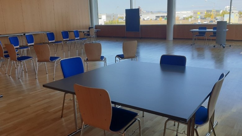 An empty seminar room with tables and chairs, a wooden floor and large windows.