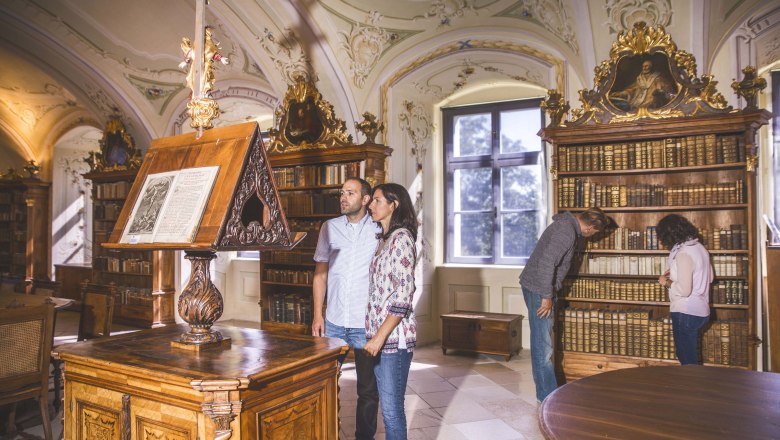 Interior view of the library in Maria Langegg Monastery with visitors and old books.