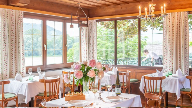 Elegant restaurant with laid tables, flowers and views of nature through large windows.