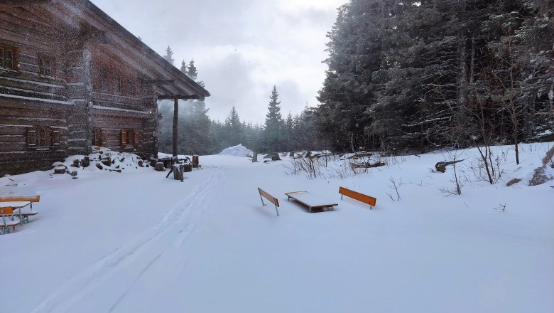 Snow-covered mountain pasture with wooden hut and benches in the winter forest.