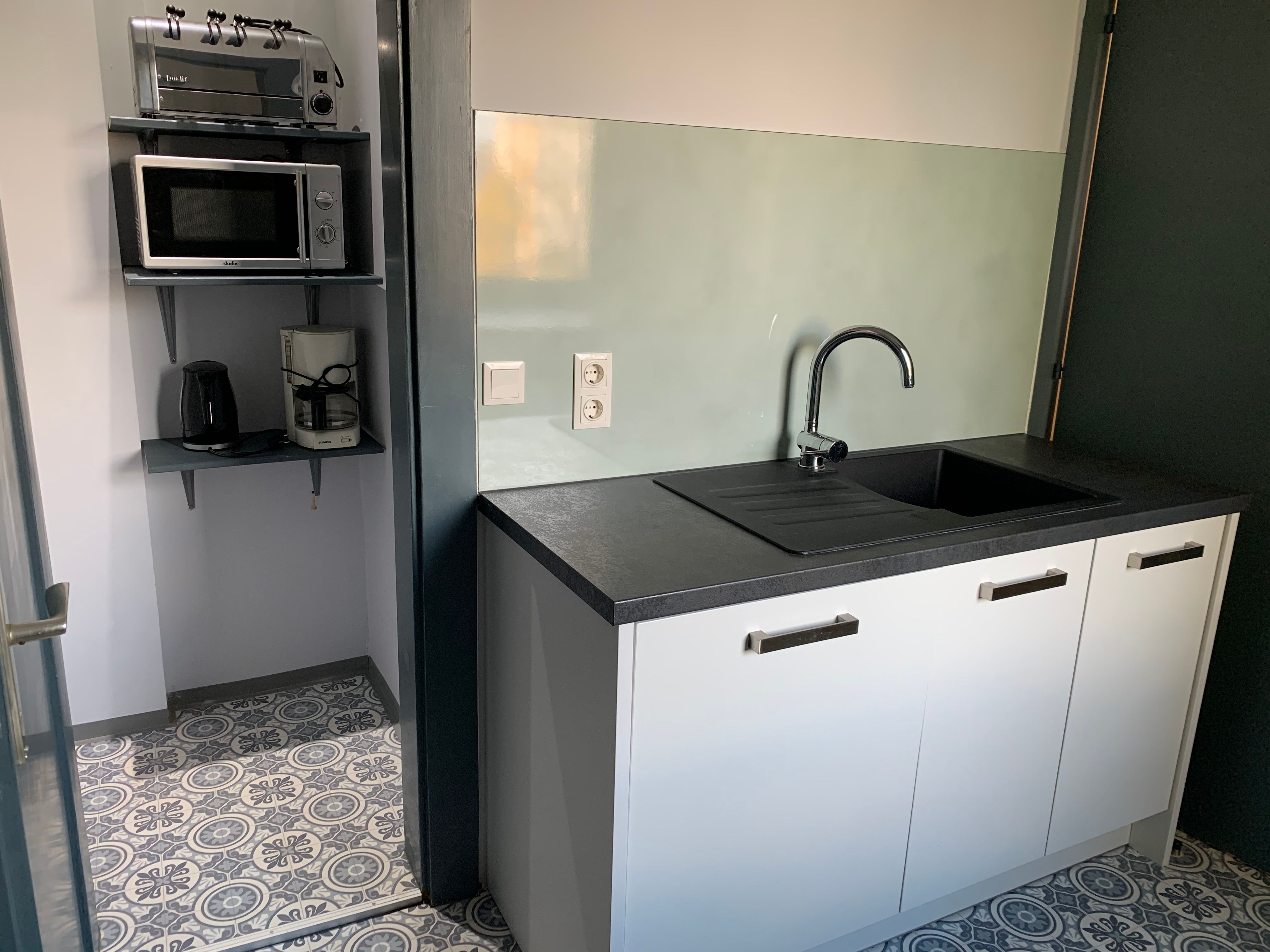 Small kitchen with sink, microwave, toaster and coffee machine.