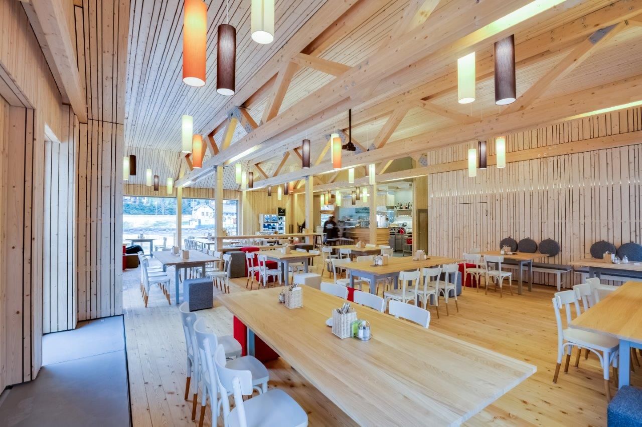 Interior view of a modern restaurant with wooden furniture and colorful hanging lamps.