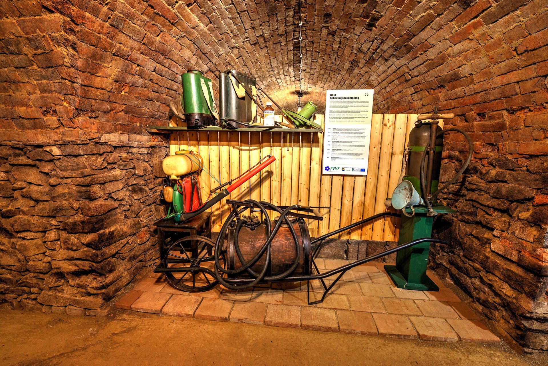 Historical agricultural equipment on display in a vaulted cellar.