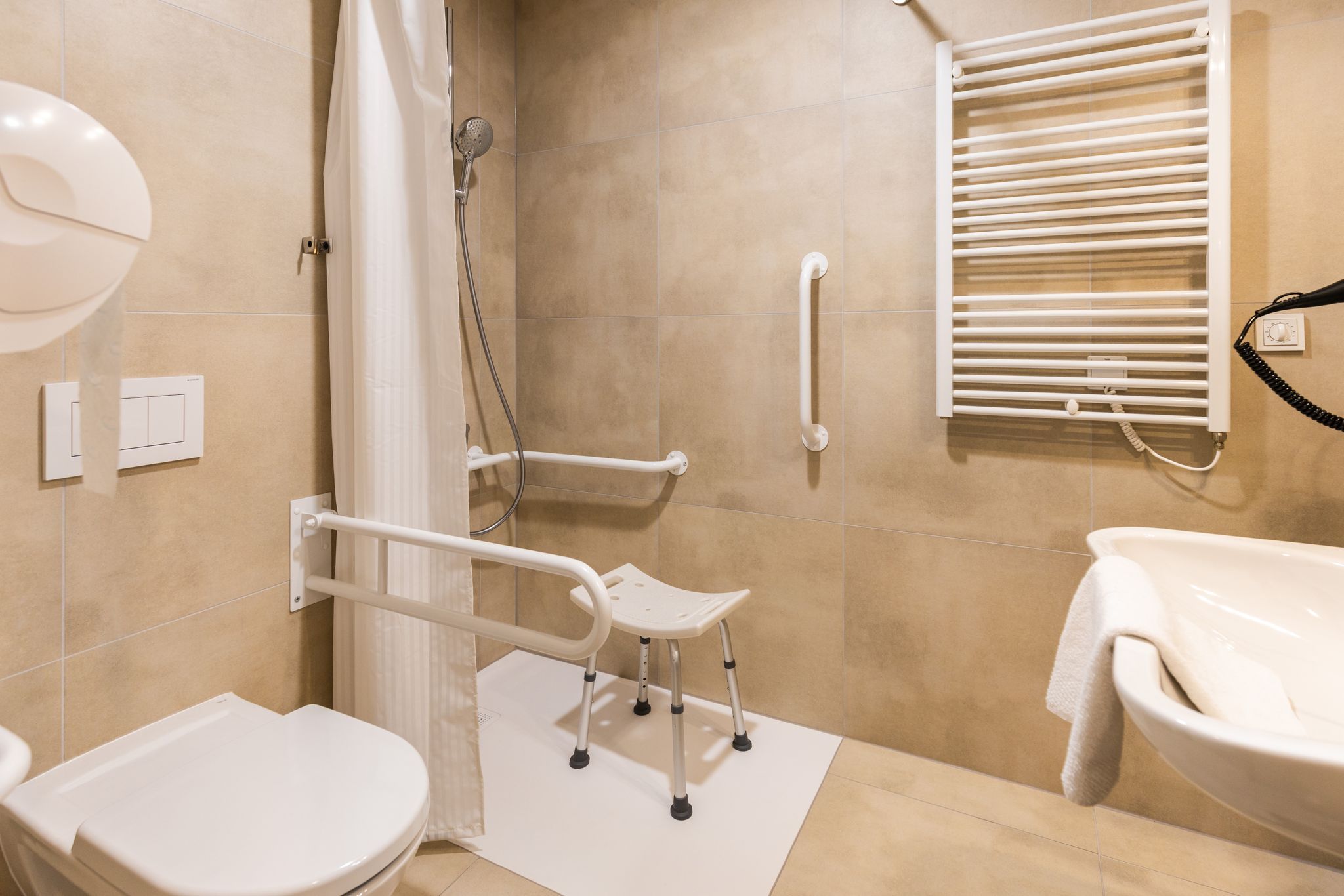 Accessible bathroom with grab bars, a shower chair, and a towel rack.