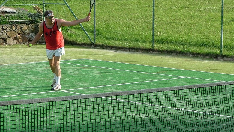 Person plays tennis on a green outdoor tennis court.