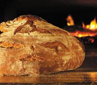 Freshly baked bread in front of a wood-fired oven with flames.