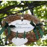 A welcome sign in a wreath with green ribbons, hung on a metal frame, against a background of green leaves.