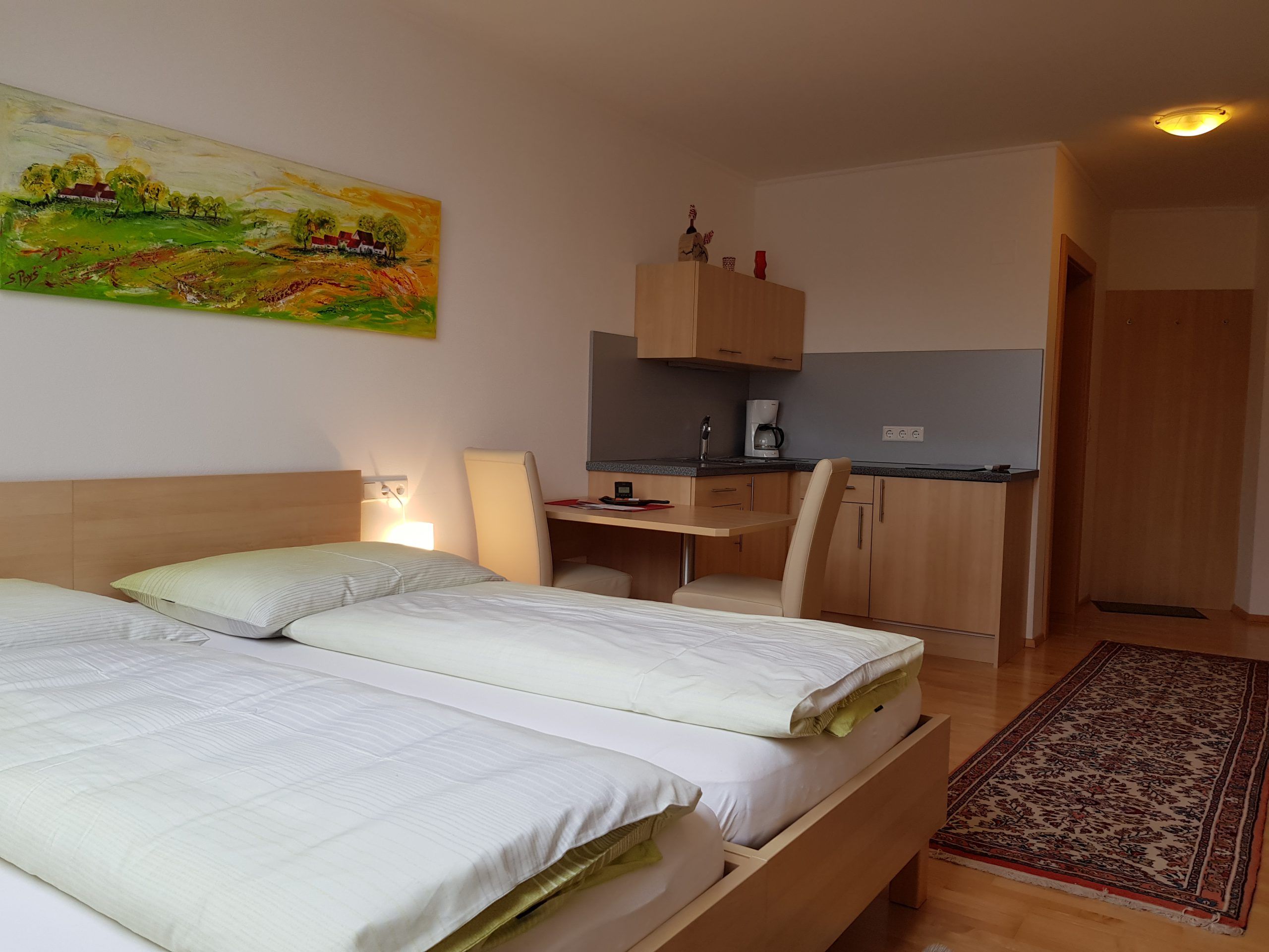 A modern room with two beds, a desk, a small kitchenette and a colorful painting on the wall.