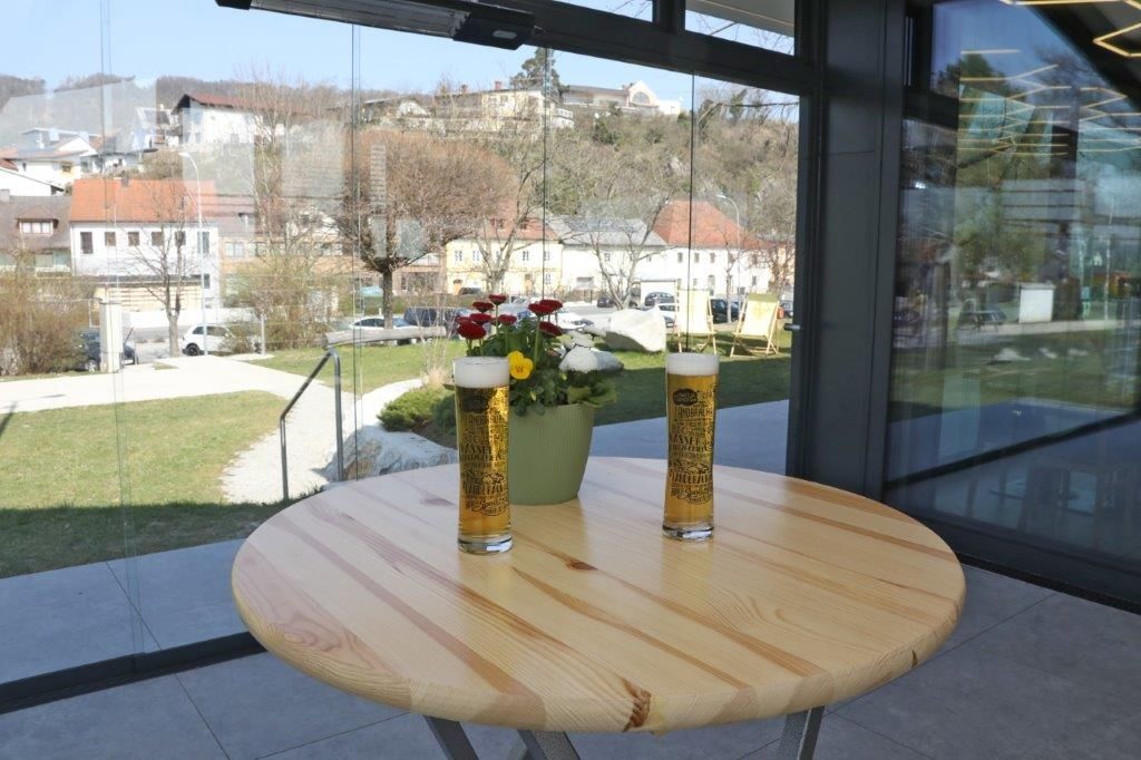 Two glasses of beer and a flower pot on a wooden table in a conservatory with a view of a cityscape.