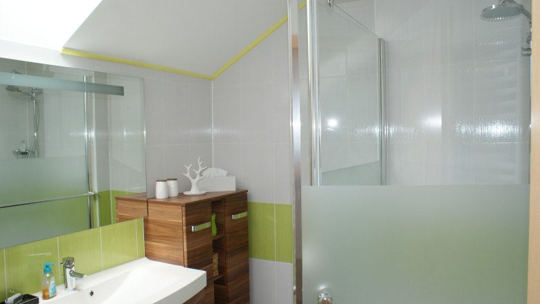 Modern bathroom with washbasin, wooden cabinet and shower with glass wall.
