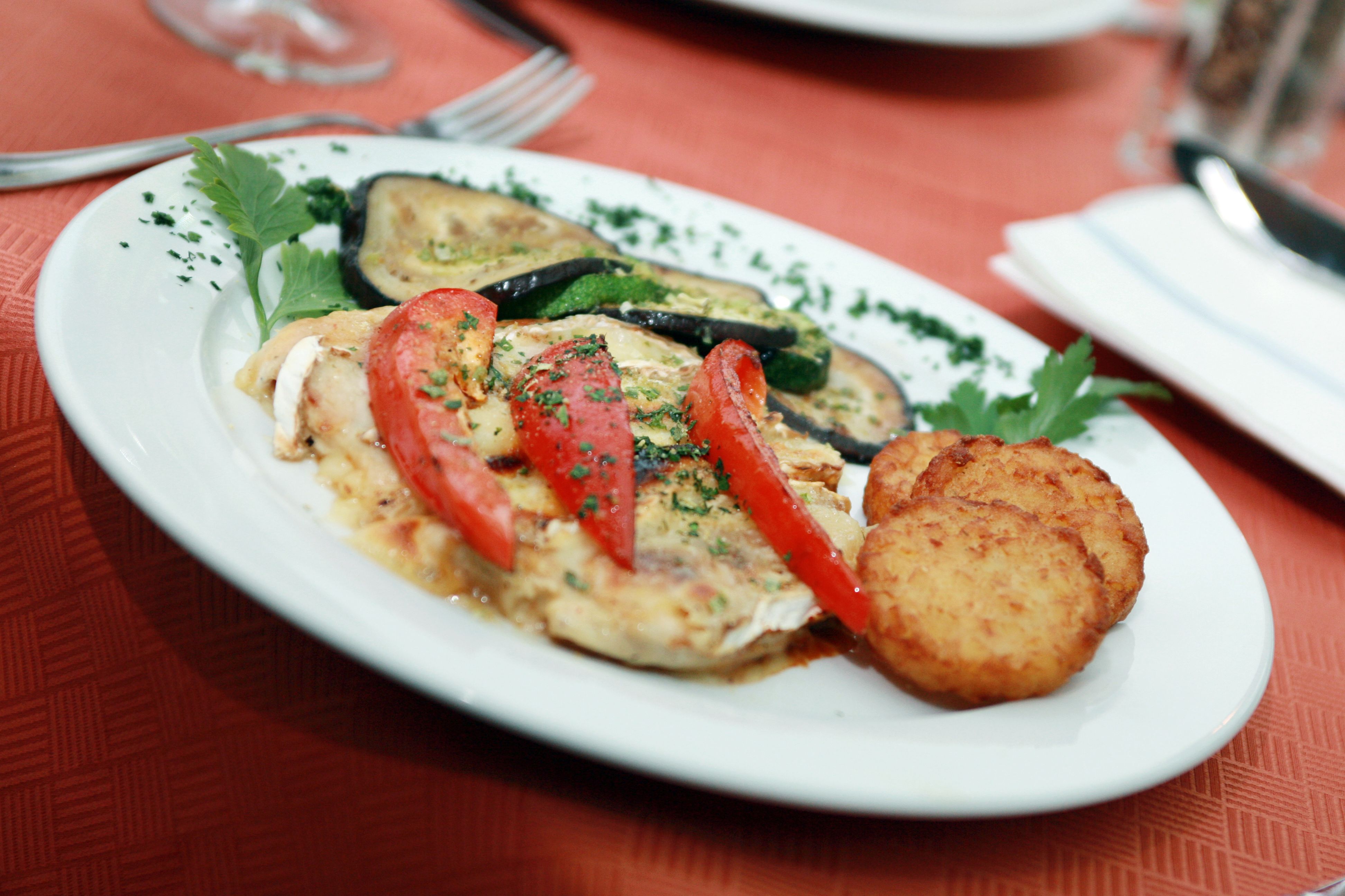 A plate of roasted vegetables, tomatoes and rösti on a red table.