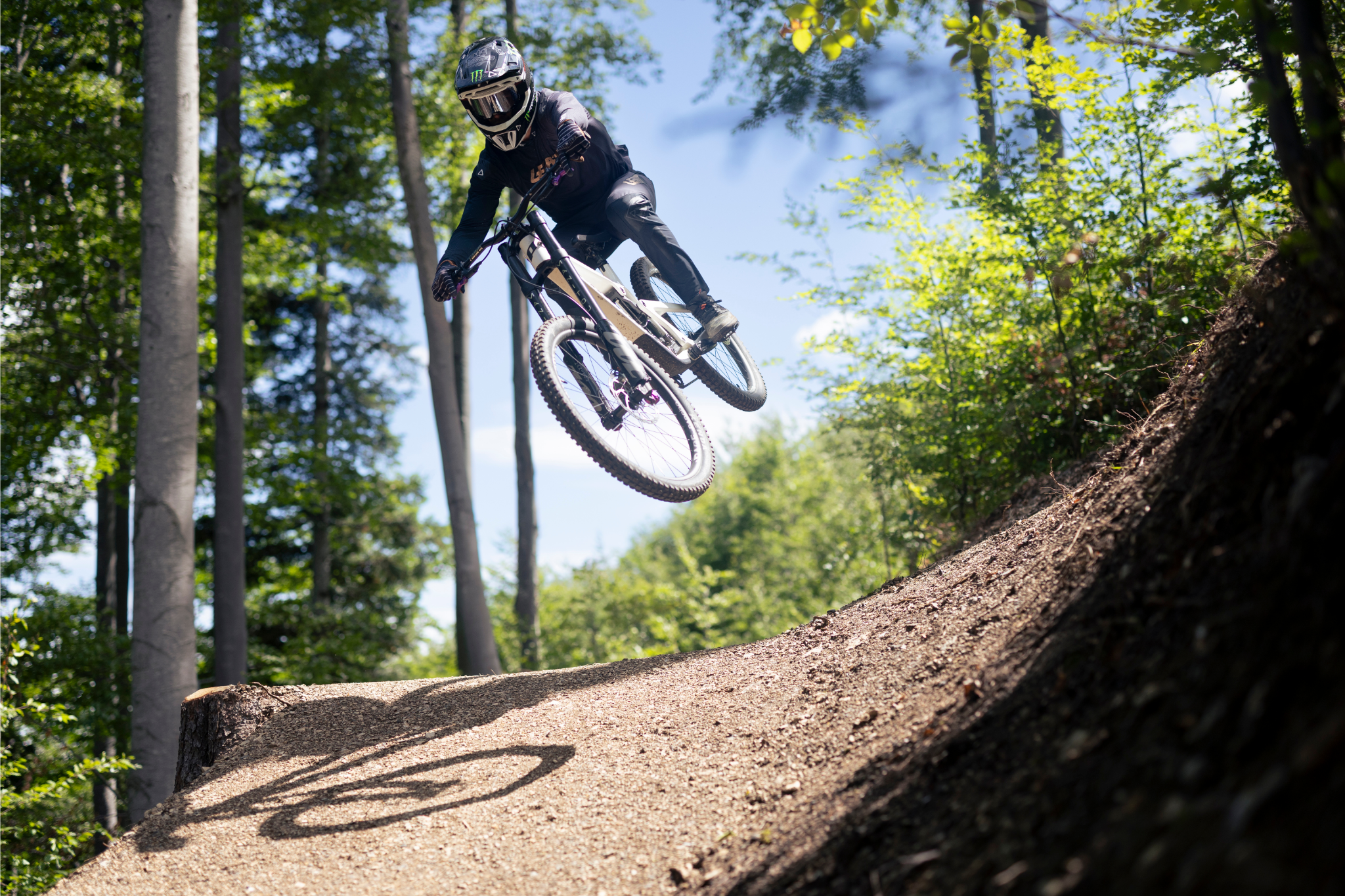 A mountain biker jumps over a hill in the forest on his bike.