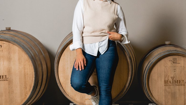 A woman leans smiling against a wine barrel at the Haimel winery.