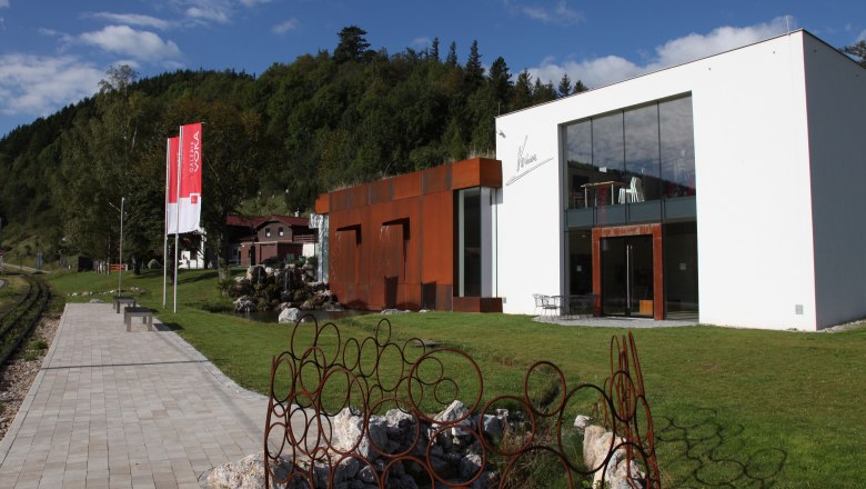Modern gallery with glass façade and rusty metal sculptures in a green setting.