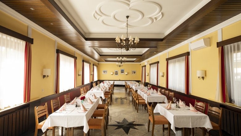 A festively decorated dining room with yellow walls, wooden furniture and white tablecloths.