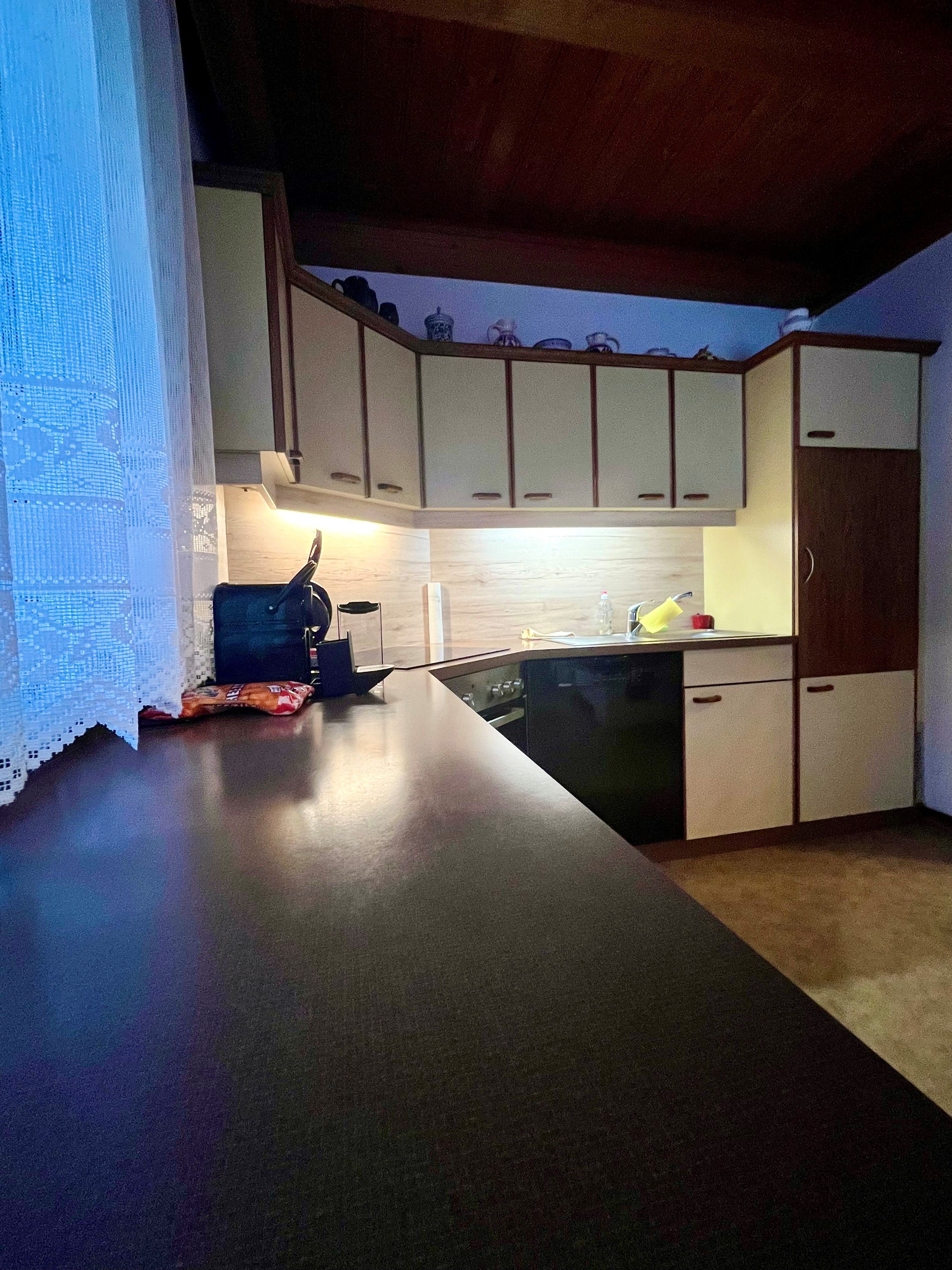 Kitchen with dark worktop, light-colored cupboards and wooden ceiling.