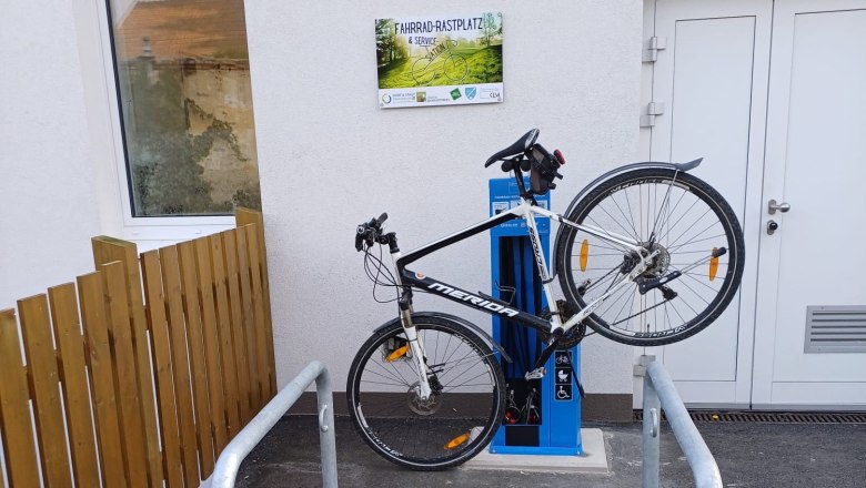Bicycle attached to a blue service station, next to a building with a 'Bicycle Rest Area & Service Station' sign.