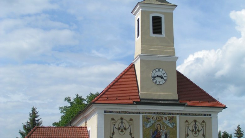 Maria Ellend pilgrimage church with tower and clock, decorated with religious motifs.