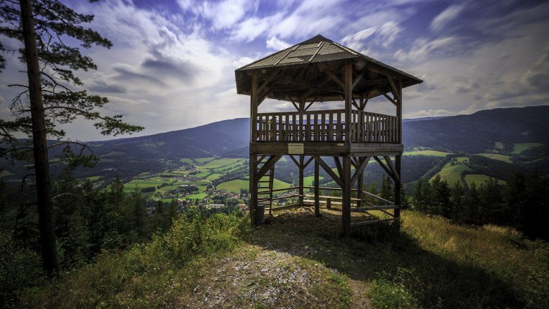 Wooden lookout tower with a view of green valleys and mountains under a blue sky.