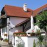 A white house with a red tiled roof, balcony and garden with plants and flowers.
