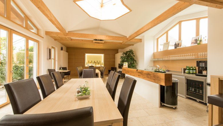Bauer family - organic winery & guest house, © foto-bauer.at Interior view of a modern tasting room with wooden tables and chairs, large windows and a bar with bottles of wine.
