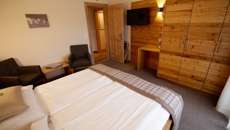 Bedroom with double bed, wooden furniture and TV on the wall.
