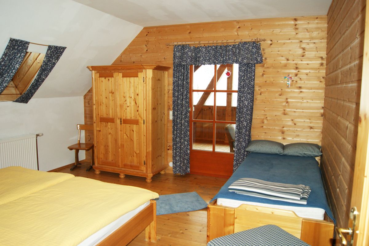 Interior view of a rustic bedroom with wooden walls, a double bed, a single bed and a closet.