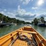 View from a wooden boat of a harbor with several boats and trees on the shore under a cloudy sky.