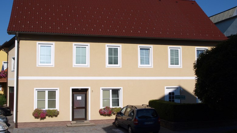 Yellow two-story house with red roof and several windows.