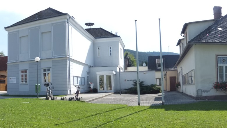 Panoramic picture of the Waidmannsfeld municipal office with surrounding buildings and cars.
