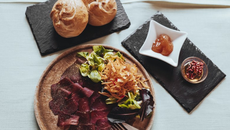 Plate with ham, salad and bread rolls on a table.