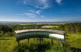 Panoramic view from a vantage point with information board, in the background a wide landscape and blue sky.