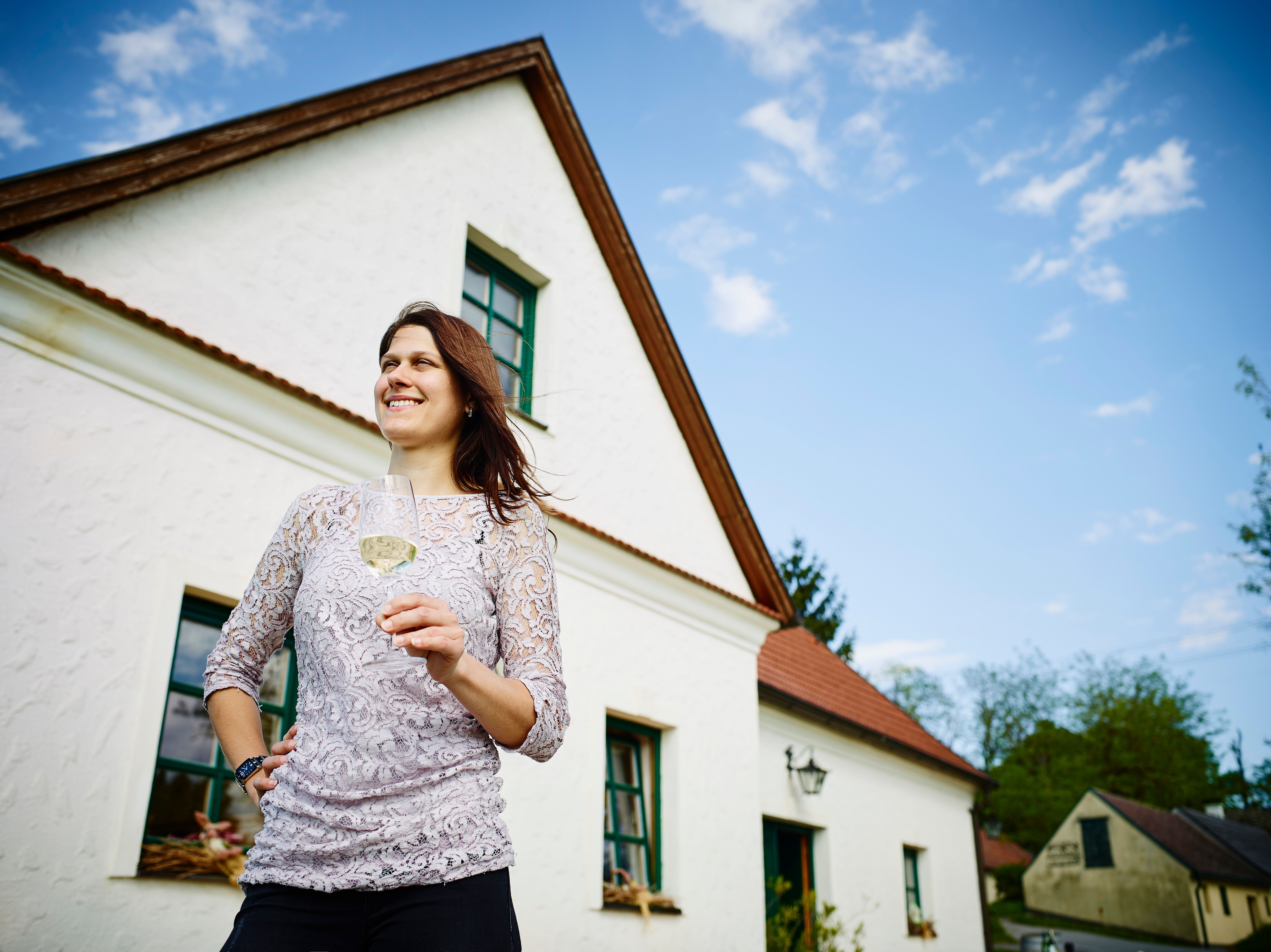 Woman with a wine glass in front of a white house with a red roof.
