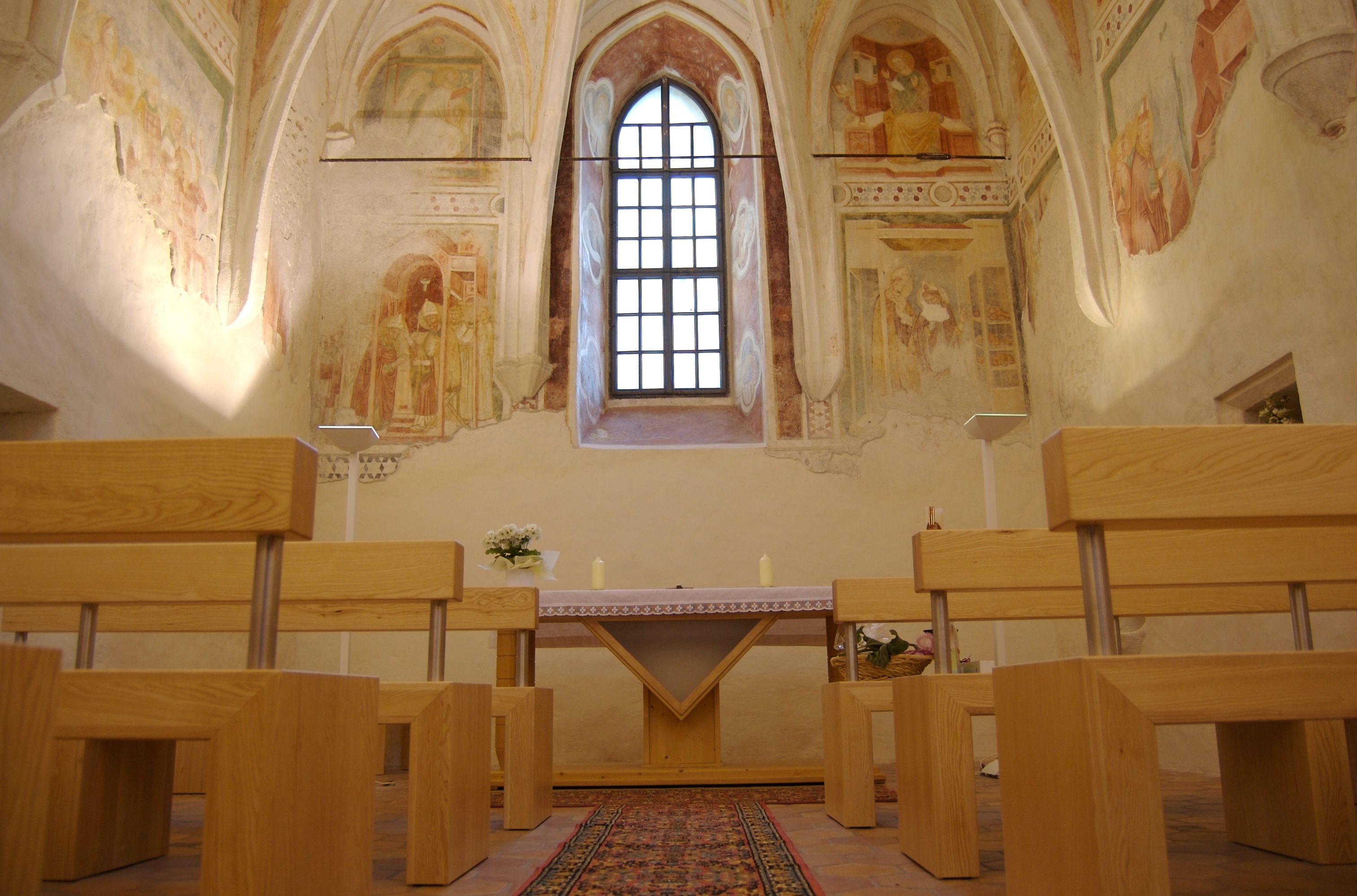 Interior view of a castle chapel with frescoes and wooden benches.