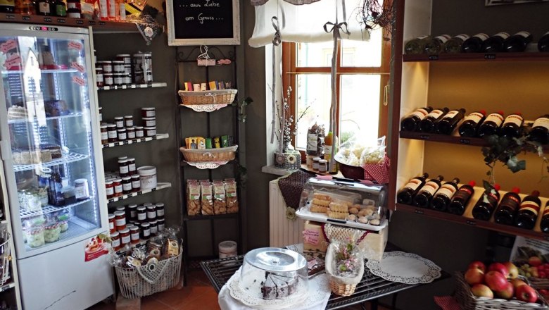 Interior view of a farm store with shelves full of bottles of wine, jams and pastries.