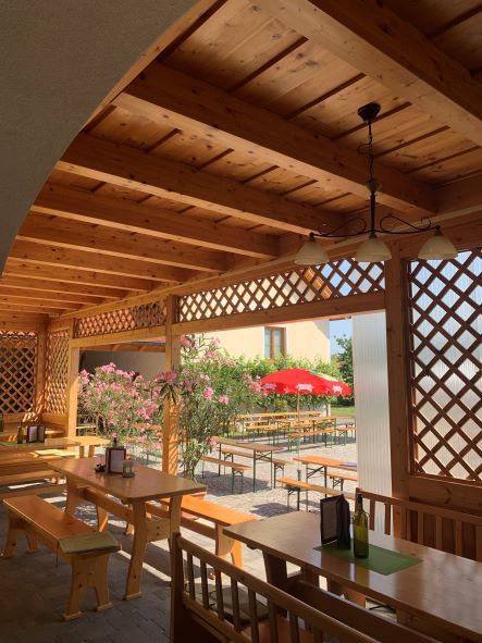 Wooden pergola with tables and benches, view of a garden with red parasols.