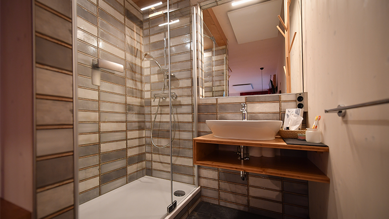 Modern bathroom with shower, washbasin and wooden shelf.