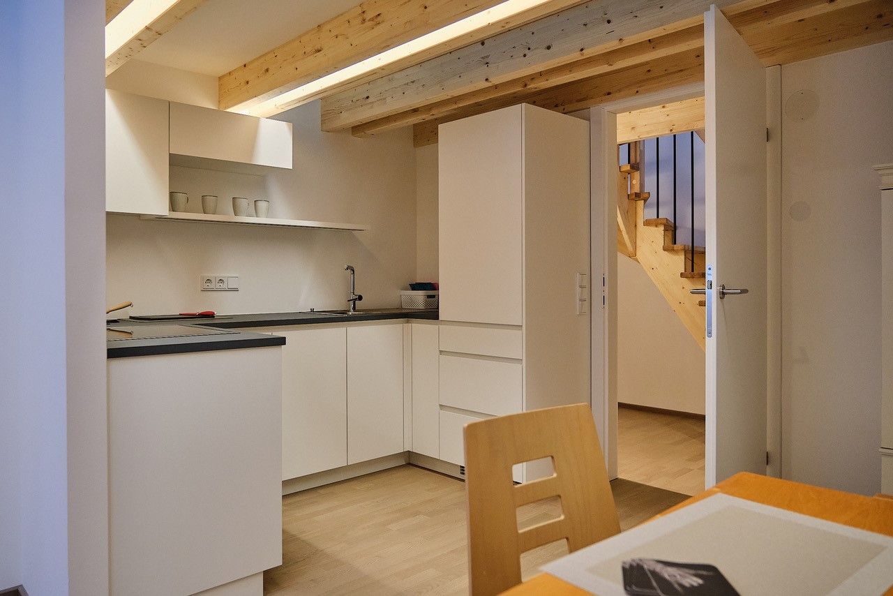 Modern kitchen with white cupboards, wooden ceiling and open access to a staircase.