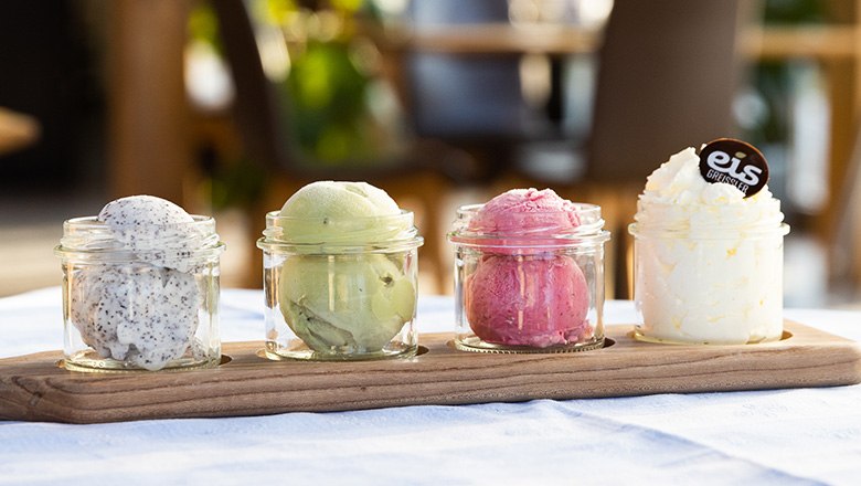 Four glasses with different types of ice cream on a wooden board.