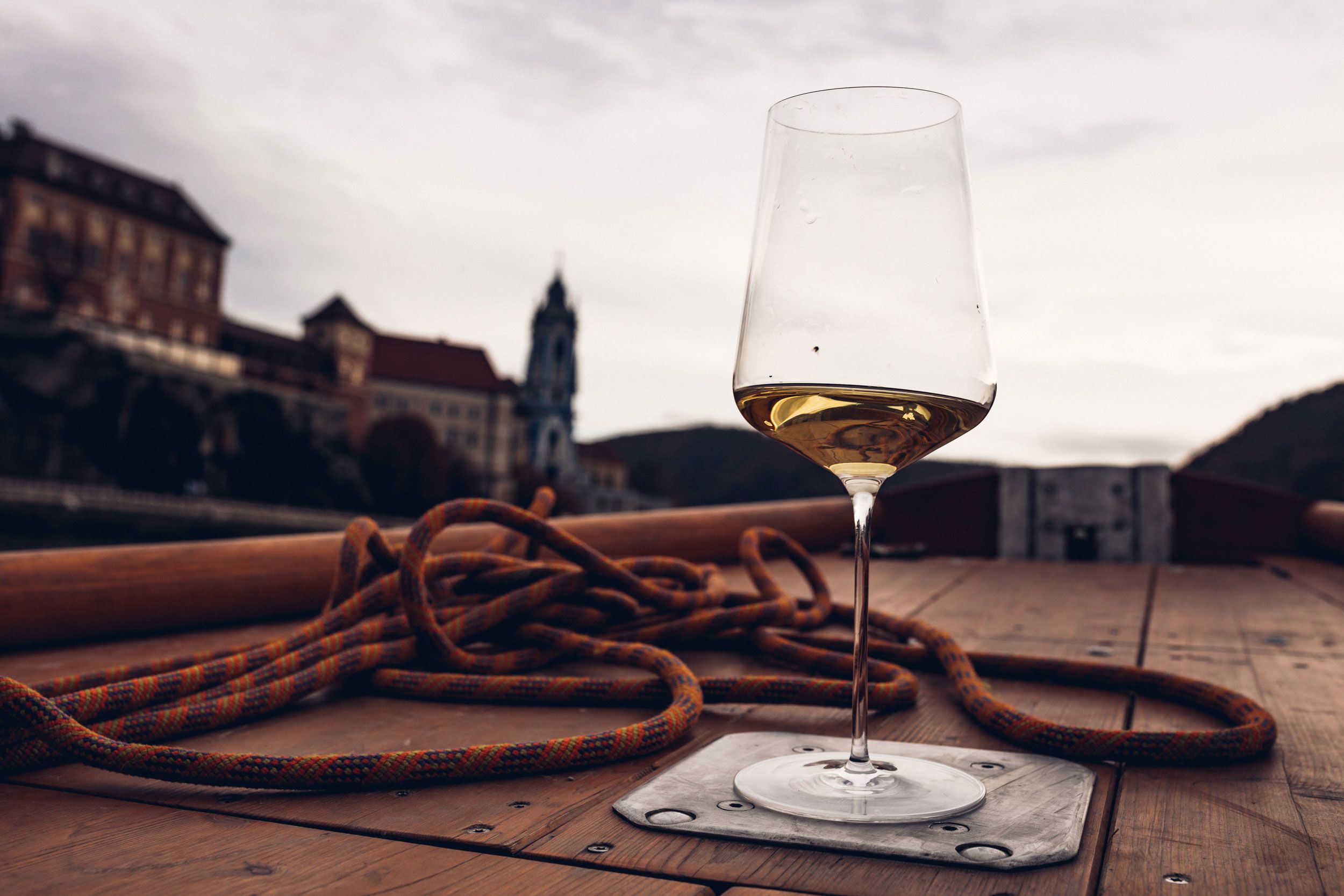 A wine glass with white wine stands on a boat, the church of Dürnstein is blurred in the background.