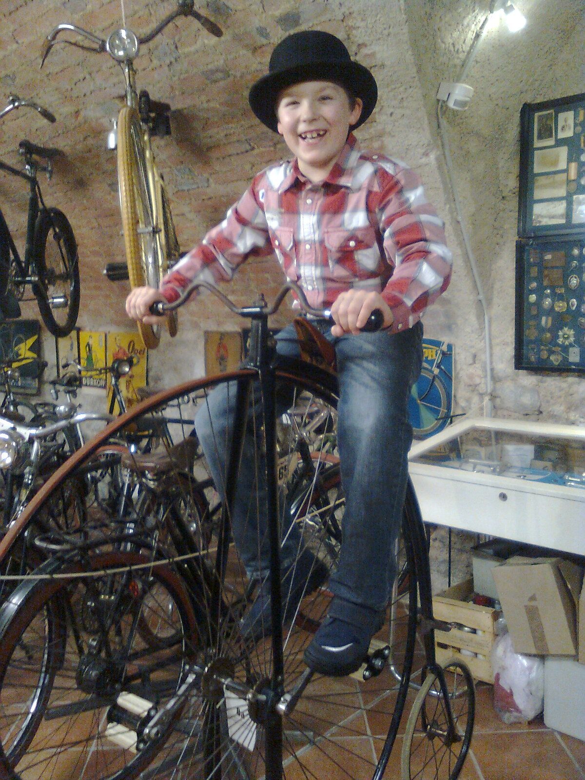 A boy with a hat sits on a penny-farthing in the Vösendorf Castle Bicycle Museum.