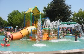 Children play in a water play garden with slides and water fountains.
