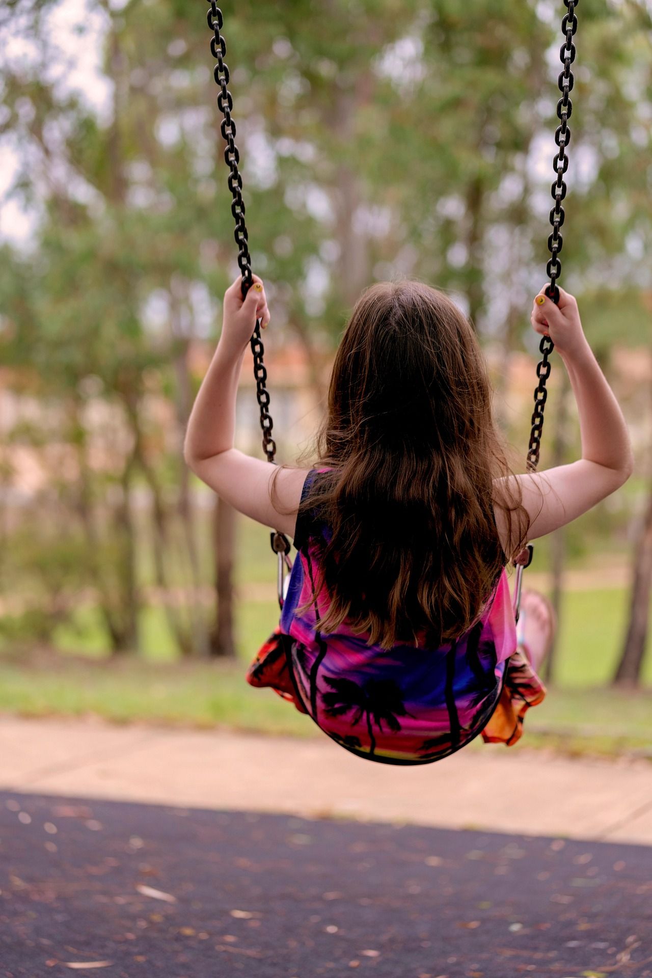 A child swings outdoors, seen from behind, surrounded by trees.